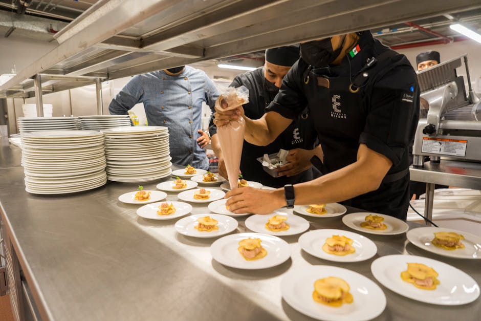 Chefs work meticulously plating gourmet dishes in a bustling professional kitchen.